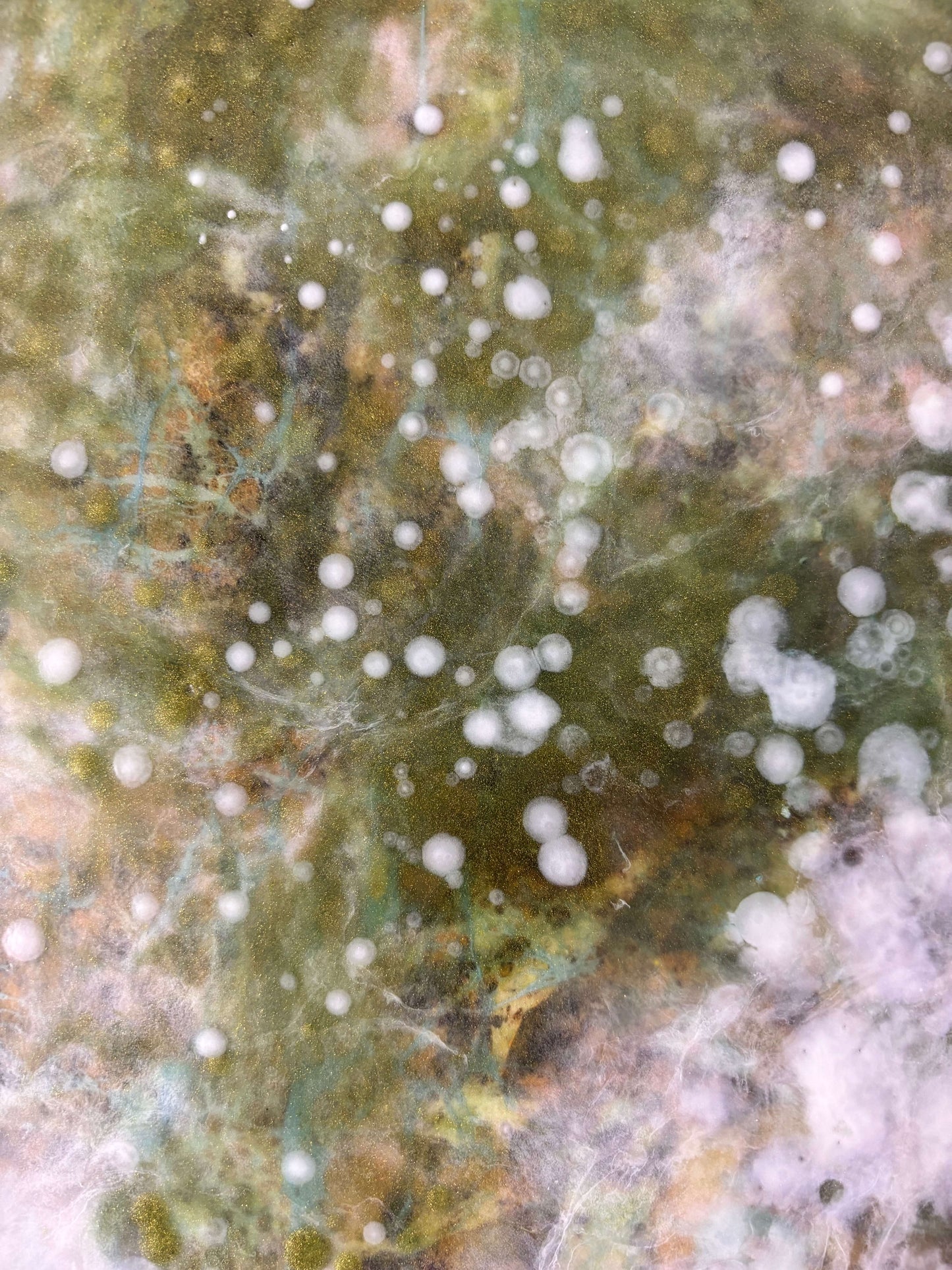 Close-up of abstract painting showing soft layers of white, green and earthy tones. textured details reveal delicate, cloud-like forms and speckled patterns that evoke nature and movement