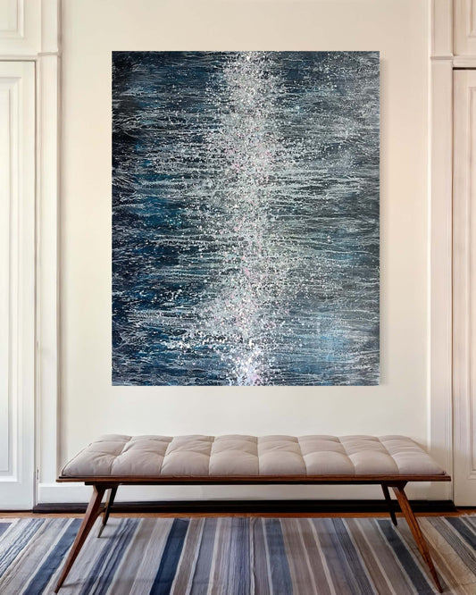 Original abstract encaustic painting in dark, moody blues with many intricate and lace like lines traveling towards the centre of the painting. Down/across the middle of this piece are a cluster of many drips and splatters of wax in pinks, white and light blue colours. Displayed above a bench in a modern foyer interior
