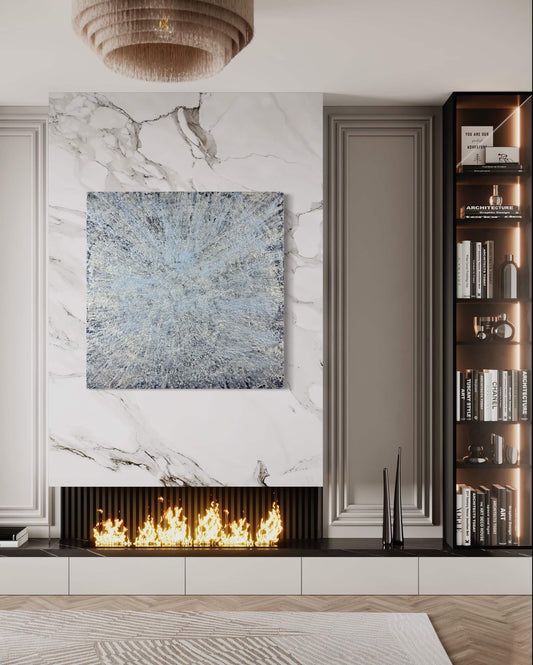 Original abstract encaustic painting is done in monochromatic tones of blues and white with layered directional textures displayed on a marble fireplace wall in a modern interior