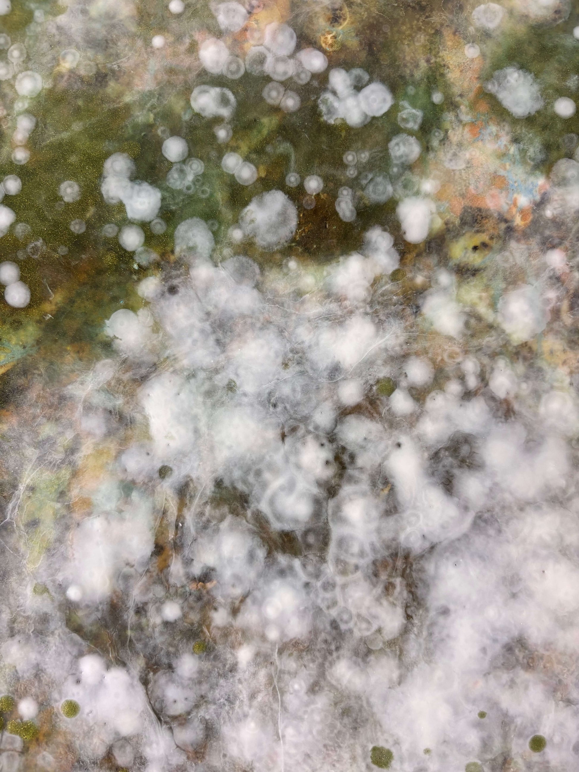 Close-up of abstract painting showing soft layers of white, green and earthy tones. textured details reveal delicate, cloud-like forms and speckled patterns that evoke nature and movement