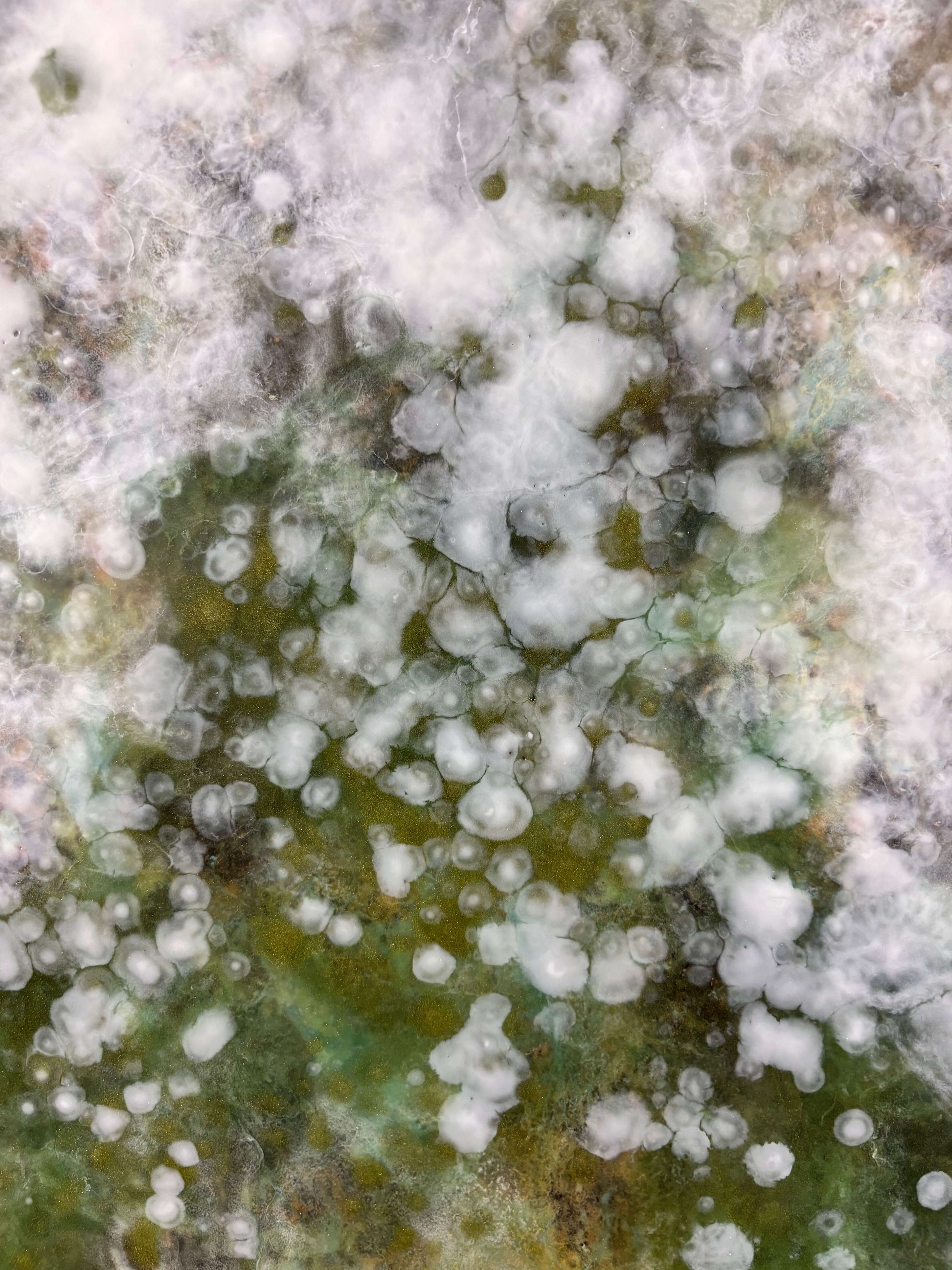 Close-up of abstract painting showing soft layers of white, green and earthy tones. textured details reveal delicate, cloud-like forms and speckled patterns that evoke nature and movement