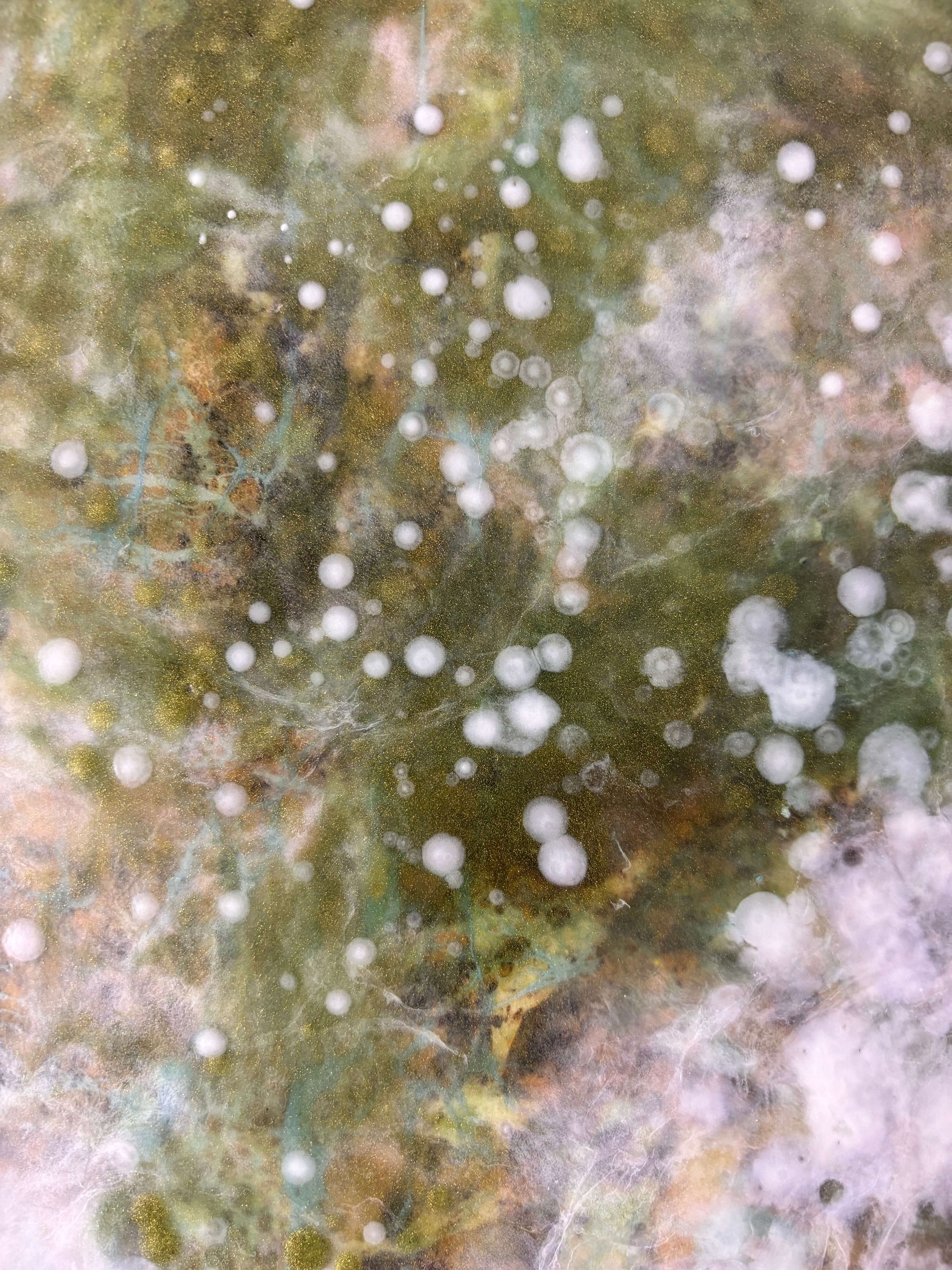 Close-up of abstract painting showing soft layers of white, green and earthy tones. textured details reveal delicate, cloud-like forms and speckled patterns that evoke nature and movement