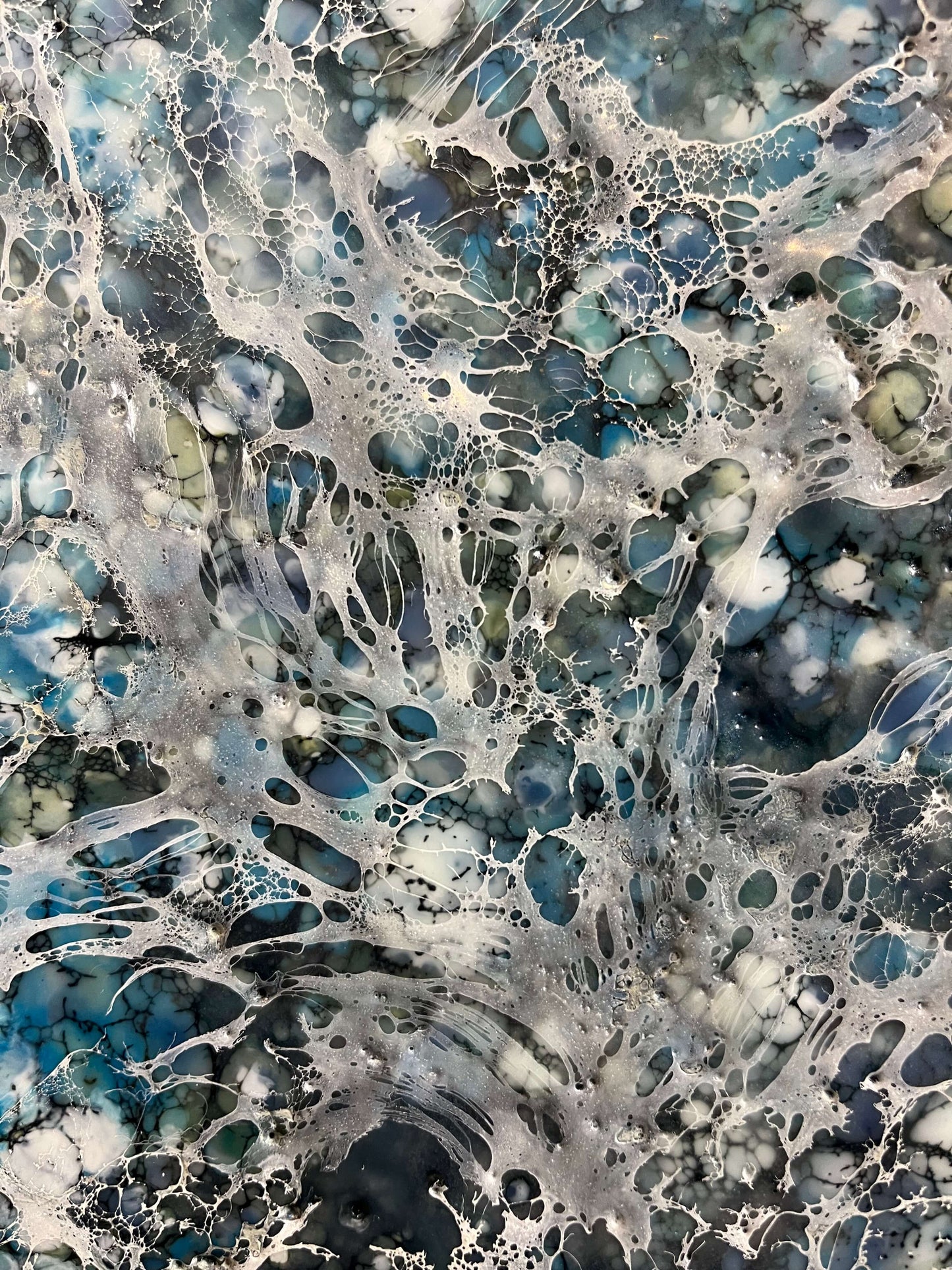 Close up.Encaustic painting in blue and white tones with lots of visual texture and many lace-like swirls. Square panel 40x40inches. It is an abstract painting, and it resembles foaming ocean waters as they hit the rocks.