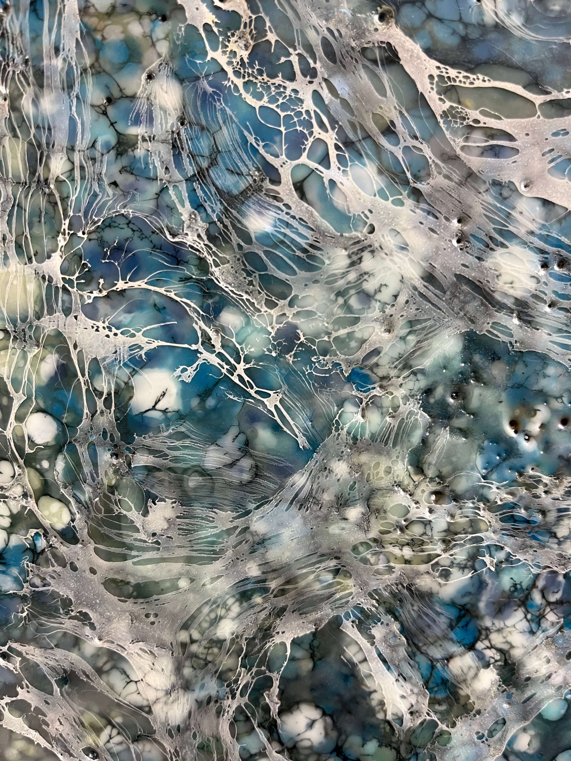 Close up.Encaustic painting in blue and white tones with lots of visual texture and many lace-like swirls. Square panel 40x40inches. It is an abstract painting, and it resembles foaming ocean waters as they hit the rocks.