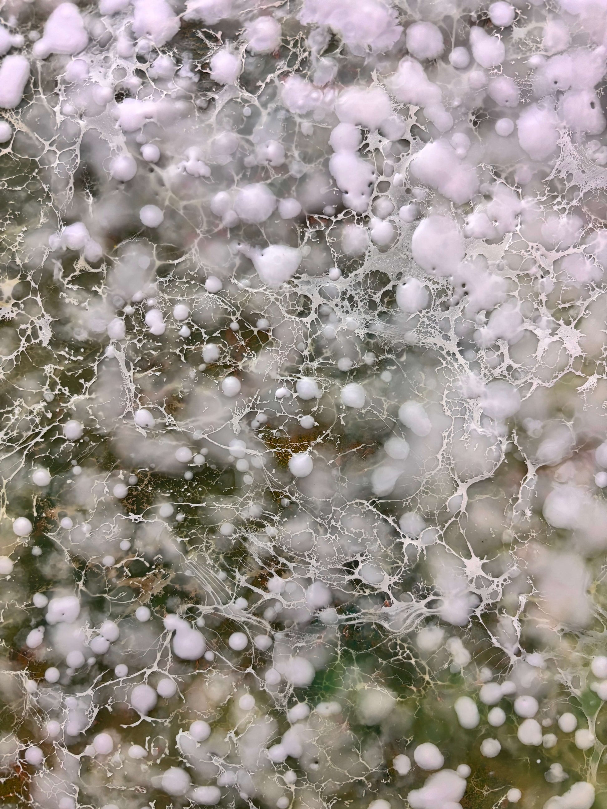 Close up.Abstract painting with delicate layers of soft white, mossy green and earthy tones. The surface is textured with fine, mist like dots, and organic forms, evoking a sense of gentle movement, growth, and natural stillness. 