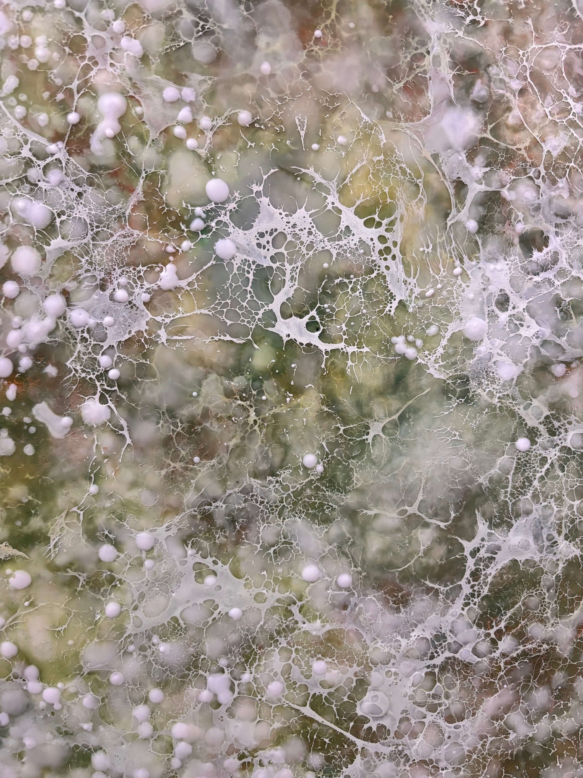 Close up.Abstract painting with delicate layers of soft white, mossy green and earthy tones. The surface is textured with fine, mist like dots, and organic forms, evoking a sense of gentle movement, growth, and natural stillness. 