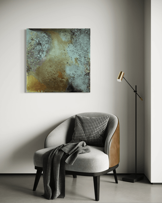 Original abstract painting in blue, grey, brown and gold tones with layered textures and organic forms displayed above  an armchair and a floor lamp in a modern interior.
